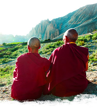 Monaci tibetani seduti volgono lo sguardo verso il paesaggio soleggiato
