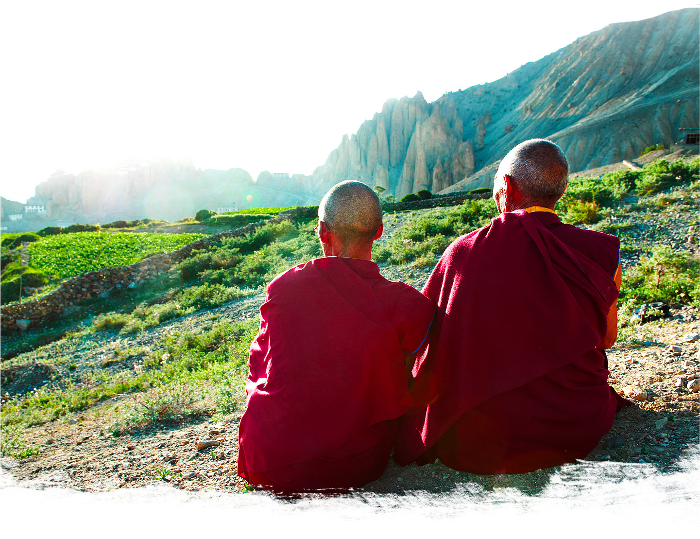 Monaci tibetani seduti volgono lo sguardo verso il paesaggio soleggiato